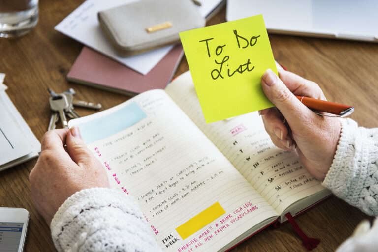 Women sitting at her desk writes her to do list in a paper diary