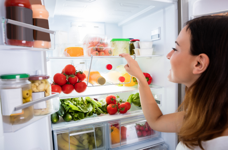 Woman looking in to clean fridge full of colourful foods