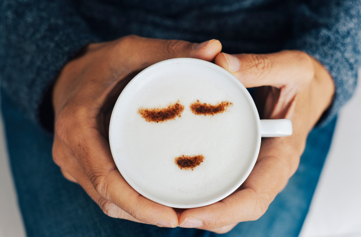 Man holding a cup of coffee with a smiley face during his fika coffee break