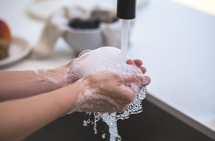Person washing hands thoroughly with soap under a tap to stay protected from illness at school
