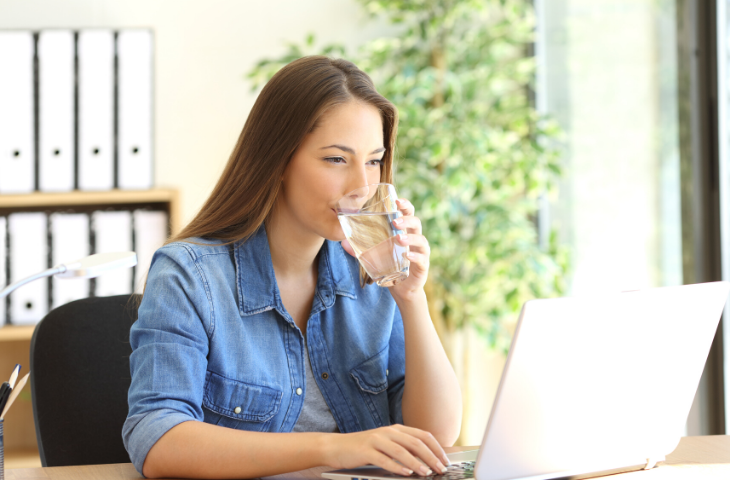 woman staying hydrated at her desk drinking water