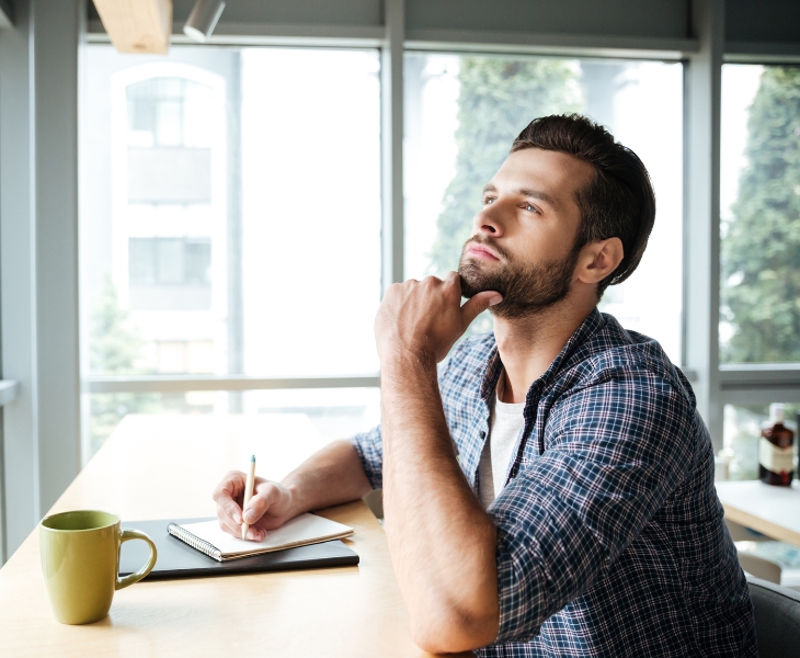 Guy sitting, thinking, and writing in a notebook