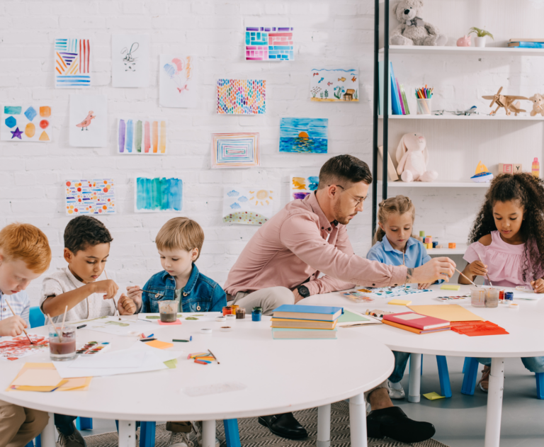 Teacher and children drawing together at tables in classroom